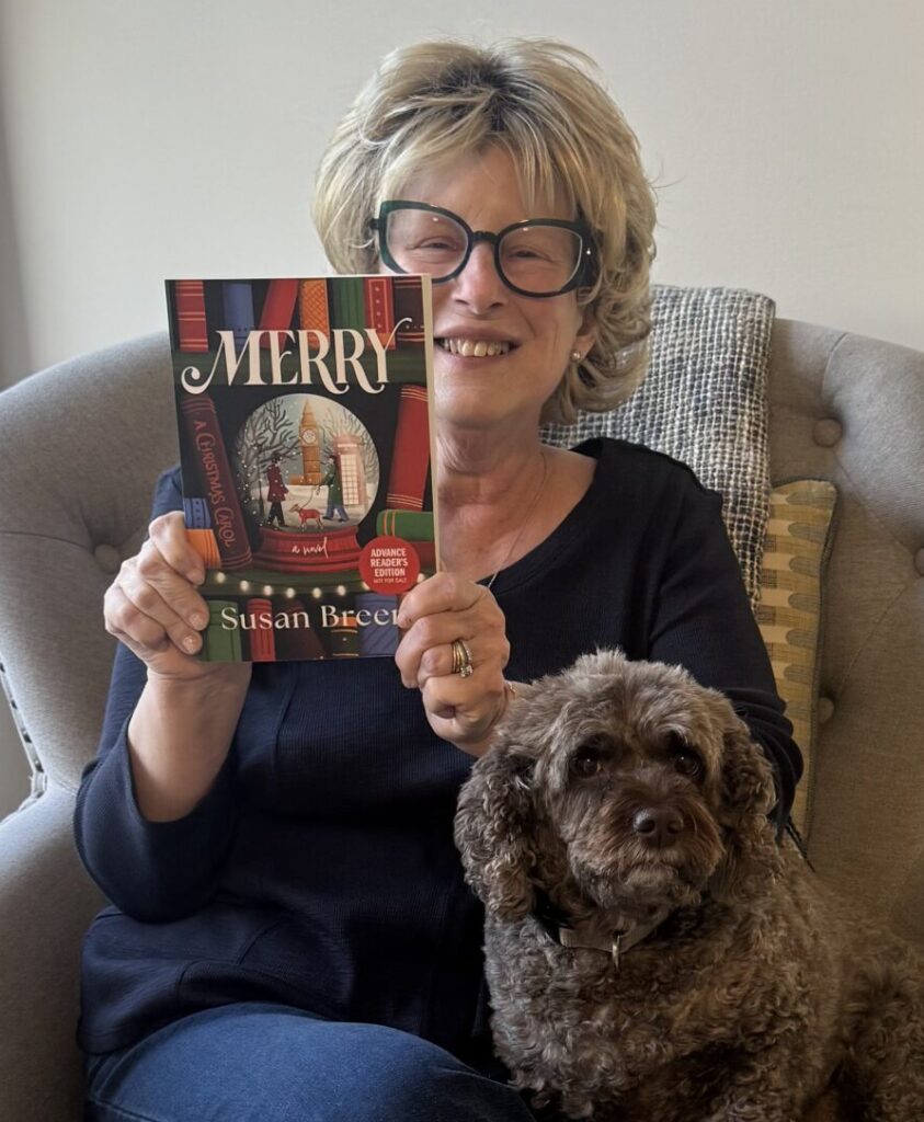 Author Susan Breen smiling while holding her new book Merry, seated in an armchair with her dog on her lap.
